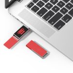 A red Milan LED flash drive is connected to a laptop, with another red flash drive nearby. The product features a logo.