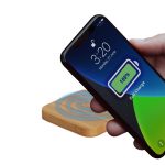 A wireless charger with a bamboo base is shown, with a phone displaying a full battery charge.