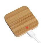A square bamboo wireless charger in a natural wood finish with a white charging cable connected.