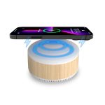 A bamboo-textured wireless charging speaker with a glowing blue top and a smartphone placed above it.