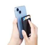 A black magnetic card wallet is being held against a smartphone, with credit cards inserted into the wallet.