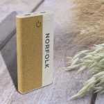 A wireless eco power bank in natural tones, featuring a logo and two USB ports on a wooden surface with grass.