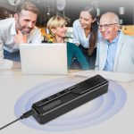 A black Akron Omnidirectional Speaker Phone is placed on a table, surrounded by four people smiling and interacting.