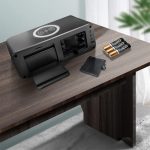 A black wireless charging speaker with a tray, batteries, and a card holder on a wooden table.