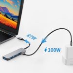 A silver USB hub with multiple ports connects to a laptop and a power adapter, displaying black cables and accessories.