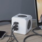 A white power cube with three USB ports and one socket, connected to devices on a wooden surface.