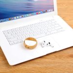 Orlando Eco TWS Earbuds in white, placed next to a laptop on a wooden surface, with a circular accessory nearby.