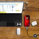 A fast charge and data sync LED cable connects a phone to a laptop on a wooden surface, with earbuds nearby.