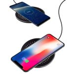 A black wireless charger with two smartphones positioned on it, displaying charging indicators on their screens.