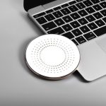A round, white wireless charger with a dotted pattern, placed next to a laptop keyboard. The charger has a metallic edge.