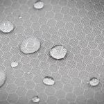 A textured grey fabric with a honeycomb pattern, featuring droplets of water on its surface.