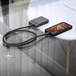 A black magnetic wireless power bank connected to a phone on a glass table. The power bank has a sleek design.