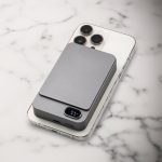 A grey magnetic wireless power bank rests on a smartphone, displaying a sleek and modern design against a marble background.