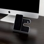 A sleek black and silver wireless charging stand for a phone and other devices, positioned next to a computer.