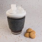 A reusable coffee cup with a white snap lid and grey RPET band, accompanied by three small cookies.