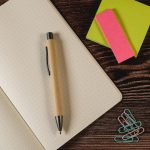 A beige pen on a dotted notebook, surrounded by colourful sticky notes and paper clips.