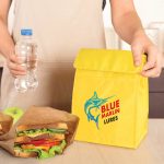A yellow cooler lunch bag with a logo, alongside a water bottle and sandwiches in brown paper bags.