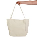 A hand holds a large, cream-coloured tote bag with two long handles and a simple design.