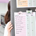 A magnetic clip in white and black, holding a colorful to-do list on a board, featuring a logo.