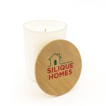 A medium glass candle with a wooden lid, featuring a logo, placed inside a white container.