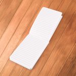 A white bamboo notebook featuring lined pages, opened to display its interior on a wooden surface.