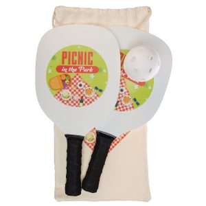 A pickleball set featuring two paddles with colorful picnic-themed graphics and a ball, enclosed in a beige storage bag.