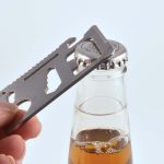 A silver multi-tool is positioned over a bottle cap, ready to open a beverage.