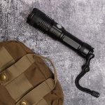 A black rechargeable torch placed on a textured grey surface next to a brown tactical bag.