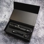 A black rechargeable torch with a charging cable, sitting inside a black box with cushioning.