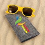 A pair of yellow sunglasses resting on a gray case, with a colorful logo on the case.