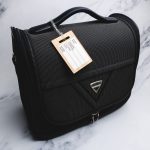 A black travel bag with a bamboo luggage tag attached, featuring a logo on the front.