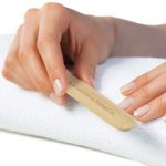 A bamboo nail file held in a hand, resting on a white towel, with natural-looking nails. It features branding.