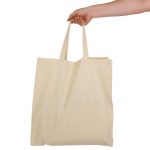 A hand holds a cream-coloured calico bag with short handles, featuring a simple design and no visible branding.