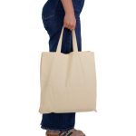 A beige reusable calico bag with short handles, held by a person in blue jeans.