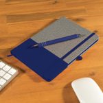 A grey notebook with a blue cover, paired with a blue pen, rests on a wooden desk near office accessories.