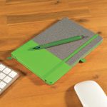 A notebook with a gray cover and green accents, accompanied by a matching green pen, placed on a wooden desk.