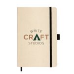 A beige A5 notebook with a black elastic band and a logo featuring the words "WRITE CRAFT STUDIOS."
