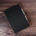 A black A5 notebook with a pen holder, featuring a minimalist design and a textured cover.