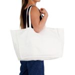 A large white reusable grocery bag held by a person, featuring two straps and a simple design.