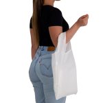 A woman holding a white reusable grocery bag while wearing a black top and light blue jeans. The bag has a logo.