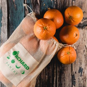 A mesh produce bag containing multiple oranges, with the words "Orchard Pantry" printed on the side.