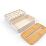 A cream-colored eco lunch box with a bamboo lid and an insert containing utensils.