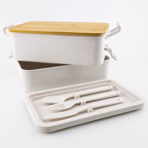 A dual-compartment lunch box in white with a gold lid, featuring a tray and cutlery set in white.