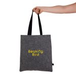 A grey felt tote bag with black straps is held by a hand, featuring a logo design.