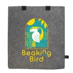 A grey felt tote bag with a colourful graphic featuring a bird, plants, and sun. It has two black handles.