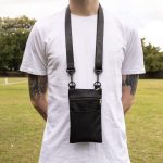 A black neck pouch with a strap, featuring a zippered pocket, worn by a person in a grassy outdoor setting.