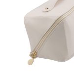 A cream toiletry bag featuring a gold zipper and a branded tag. The bag has a geometric shape and smooth finish.