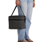 A grey cooler bag with a handle, held by a person wearing light blue jeans and casual shoes.