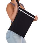 A person holding a black Cosi Wet Bag with a white zip and shoulder strap. The bag appears spacious and lightweight.