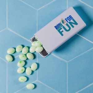 A flip top tin filled with light green spearmint mints is shown, with some mints scattered around.